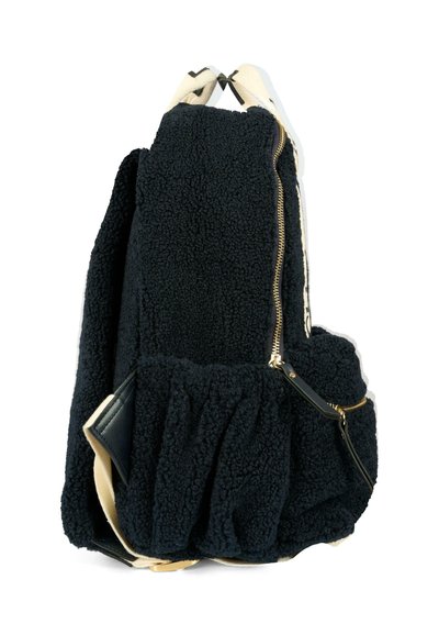 Zaino in pile nero con superficie testurizzata, zipper dorato, spallacci color crema e dettagli in pelle scura. Presenta una sezione inferiore arricciata.