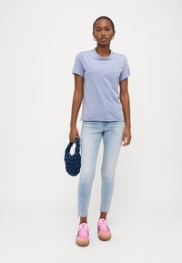 Tricou crew-neck violet deschis, blugi skinny bleu deschis, adidași roz cu accente negre și o geantă împletită bleu închis.