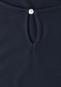 Tissu en maille bleu marine avec une petite ouverture ovale en forme de trou de serrure, fixée par un bouton argenté rond en haut au centre.