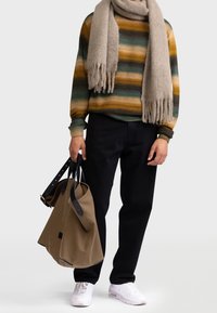 Sweter dziewiarski w zielone, żółte i brązowe paski; szary szalik; czarne spodnie; niesie brązową torbę z czarnymi paskami; białe sneakersy.