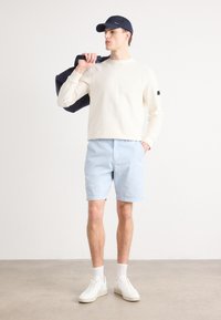 Sweatshirt leve e suave, calções azuis claros, sapatilhas brancas, boné azul marinho, segurando uma bolsa azul marinho. Design simples com detalhes mínimos.