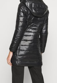 Abrigo acolchado negro con un acabado brillante, que cuenta con capucha, diseño acolchado vertical y una silueta ligeramente entallada para un ajuste ajustado.