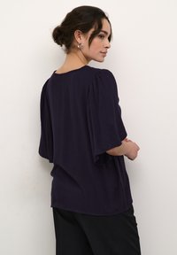 Lilla tekstureret bluse med korte, brede ærmer og en afslappet pasform. Designet har bløde linjer og en subtil mønstrede overfladedetalje.