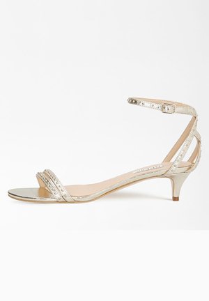 Złote metaliczne sandały z dwiema poziomymi paskami i regulowanym paskiem na kostkę. Oferują niski obcas w kształcie kociego pazura oraz gładką, błyszczącą teksturę.