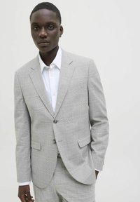 Traje de cuadros gris claro que presenta un blazer ajustado con dos botones, solapas de muesca y pantalones a juego, complementado con una camisa blanca de botones.