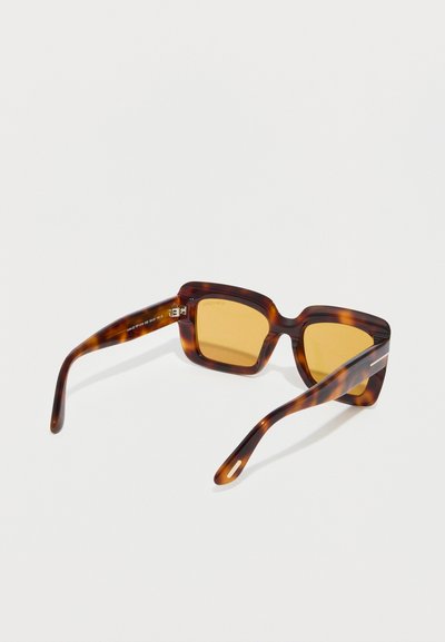 Ορθογώνια γυαλιά ηλίου με σχέδιο χελώνας και φακούς με κεχριμπαρένιο χρώμα, ελαφρώς κεκλιμένα σε λευκή επιφάνεια.