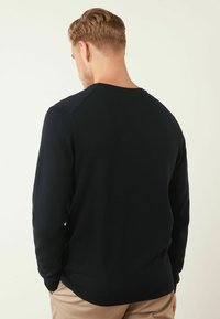 Pull en tricot doux bleu marine foncé, avec un col rond et des poignets côtelés. Design simple et minimaliste avec une finition soignée.