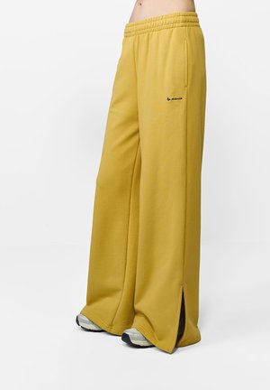 Žlté, široké tepláky s elastickým pásom, bočnými vreckami a rozparkom na spodnom leme. Obsahujú malý čierny detail loga.