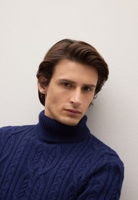Navy blue cable-knit sweater with a high ribbed turtleneck, featuring a textured pattern and a close-fit design.