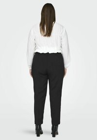 Vit, texturerad blus med smockad midja, i kombination med svarta, skräddarsydda byxor och svarta, klackade ankelstövlar. Vy tagen bakifrån.