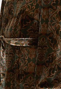 Πράσινο βελούδινο ύφασμα με προηγμένα καφέ λουλούδια και σπείρες, με λεπτομέρεια στη μέση που δένει. Μαλακή υφή, πολυτελής εμφάνιση.