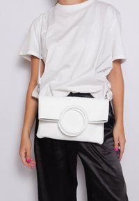 Borsa a tracolla bianca in pelle con finitura testurizzata, accento frontale circolare e chiusura a pattina. Tracolla regolabile per un trasporto versatile.