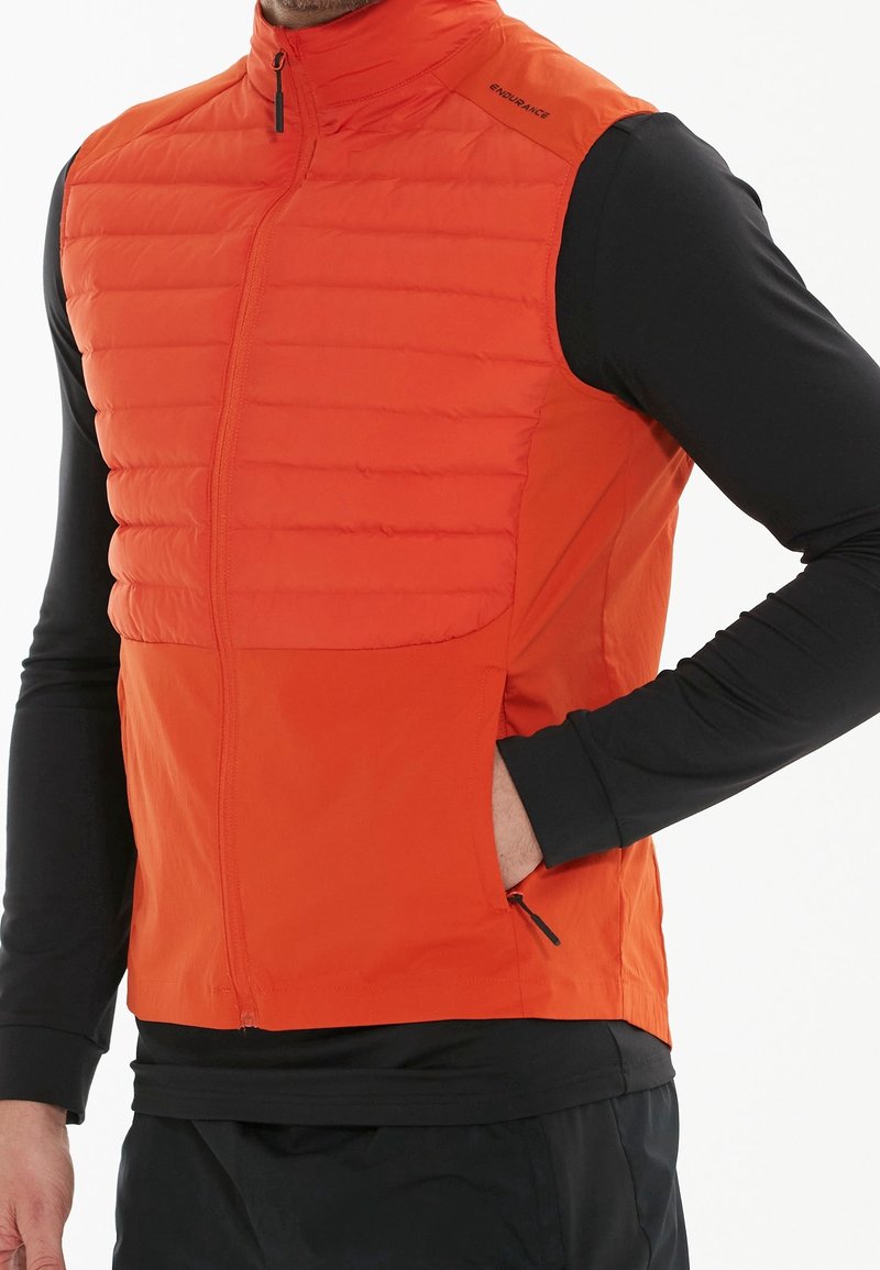 Herrarnas orange ärmlösa väst med vadderad front, hög krage och dragkedjefickor. Lättviktigt tyg med en slät textur och en figursydd design.