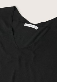 Pull noir en V avec une texture lisse, comportant un col légèrement côtelé et une étiquette d'entretien visible à l'intérieur.