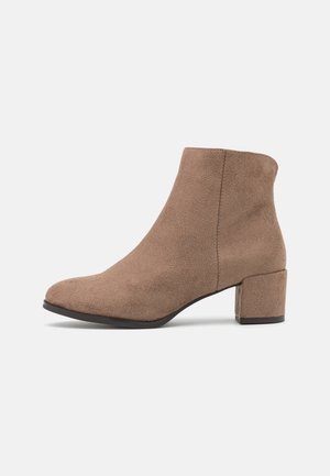 Bruine suède enkellaars met een ronde neus en een blokhak. Gladde textuur, minimale stiksels en geen zichtbare hardware accenten.