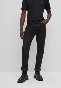 Camisa negra de algodón con un pequeño logo, combinada con jeans negros de corte slim y puños doblados. Se lleva con botas negras con cordones.