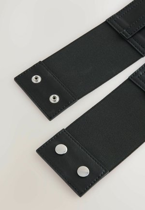 Cintura elastica nera con due estremità in pelle e chiusure a scatto in argento. Superficie liscia con cuciture robuste lungo i bordi.