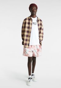 Camisa de franela en tonos púrpura y amarillo sobre una camiseta blanca; pantalones cortos tie-dye en rosa y azul; zapatillas blancas con acentos negros.