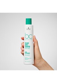Bouteille en plastique blanche avec un bouchon turquoise, présentant un texte vert. L'étiquette indique "bc Bonacure Volume Boost Shampooing Créatine", taille 250 ml.