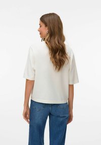 Hvid kortærmet top med en afslappet pasform og en elegant krave, parret med blå vide jeans. Glat tekstur med minimal detaljering.