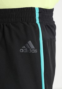 Pantalones cortos deportivos negros con una cinturilla elástica, que cuentan con una franja lateral de color azul claro y un logotipo negro de Adidas en la pierna izquierda.