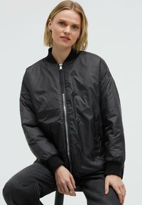 Schwarze Bomberjacke mit Reißverschluss vorne, geripptem Kragen und Bündchen, mit glatter, glänzender Textur und seitlichen Taschen.