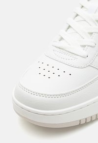 Baskets en cuir blanc avec une boîte à orteils perforée, des lacets plats et une semelle texturée. Forme arrondie avec des détails cousus et des accents de semelle clairs.