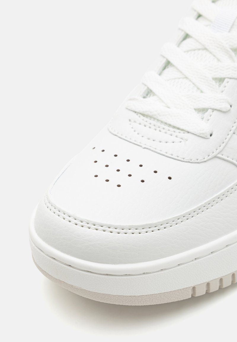 Witte leren sneaker met geperforeerde neus, platte veters en gestructureerde zool. Rond gevormd met gestikte details en lichte zoolaccenten.