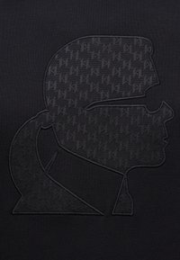 Μαύρο ύφασμα με ανάγλυφο, τόνικο σχέδιο προφίλ με γυαλιά ηλίου και κοτσίδα, τονίζοντας τις λεπτομερείς ραφές.