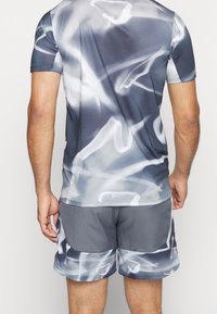 Camiseta atlética de manga corta en gris con un patrón en espiral blanco, combinada con pantalones cortos grises. Ambos artículos presentan una tela ligera y transpirable.