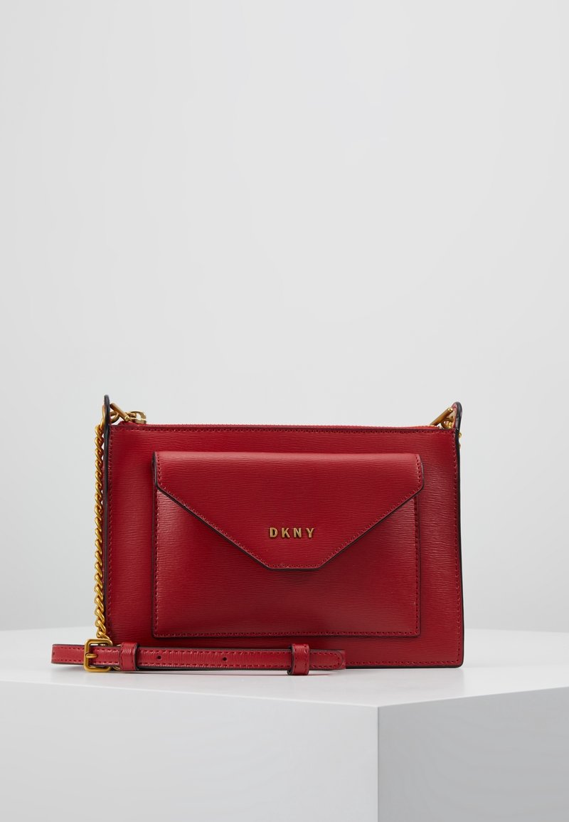 Borsa a tracolla DKNY in pelle rossa con tasca a busta frontale, tracolla in catena dorata e tracolla in pelle regolabile su superficie bianca.