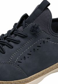 Scarpa grigio scuro con finitura in pelle liscia, ritagli decorativi, tessuto texturizzato al collare e suola leggera maculata.