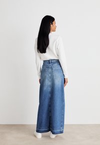 Denim maksi krilo z visokim pasom, svetlo modrim pranjem, dvema zadnjima žepoma in širokim, jersey oblikovanjem. Usklajeno z belo majico in belimi čevlji.