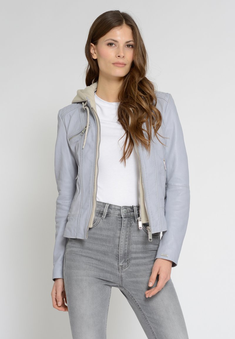 Lichtgrijze leren jas met capuchon, zilveren rits en zijzakken, gecombineerd met strakke grijze jeans en een wit t-shirt.