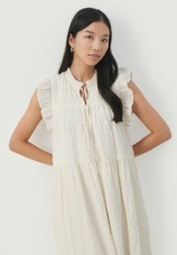 Robe blanche texturée avec des bords de manches à volants, décolleté en forme de clé et coupe ample. Présente un design froncé et à volants pour plus de volume.