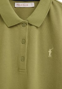 Olivengroene poloshirt met drie knopen, een klein wit geborduurd logo van een persoon die een stok vasthoudt, en een "POLO CLUB" label aan de binnenkant van de kraag.