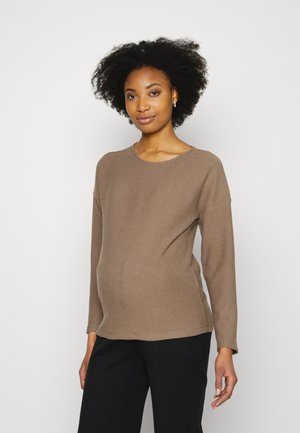 Top longo de mangas ribbed em marrom, com decote redondo. O tecido tem uma textura suave e adapta-se a uma barriga em crescimento, combinado com calças escuras.