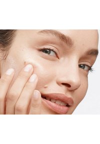 Gros plan sur un visage avec une peau lisse, un teint clair et un maquillage naturel. Des doigts touchent doucement la joue, mettant en valeur un éclat sain.