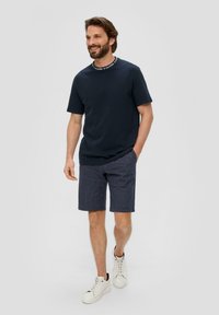 Granatowa bawełniana koszulka z kontrastowym kołnierzykiem, zestawiona z granatowymi szortami w paski i białymi trampkami. Luźny krój i teksturowany materiał.