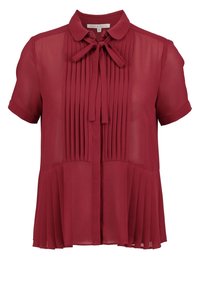 Blouse bordeaux en tissu léger et transparent avec des manches courtes. Présente des plis sur le devant et un nœud au col. Design d'ourlet accentué.