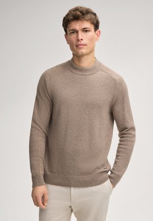 Pull en maille beige avec un col rond à côtes et des poignets côtelés. Il présente une texture douce et une coupe ajustée, idéale pour un look décontracté.