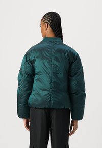 Párnázott bomber dzseki fényes sötétzöld anyagból. Bordás gallérral és oversize szabással rendelkezik, melynek bő ujjai vannak.