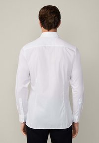 Witte blouse met lange mouwen van een gladde stof, met een standaard kraag, knoopmanchetten en een getailleerde pasvorm, weergegeven vanuit de achterkant.