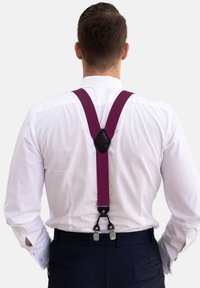 Lila elastische Hosenträger mit schwarzen Lederakzenten, gesichert mit silbernen Clips, getragen über einem weißen Hemd und navyblauen Hosen.
