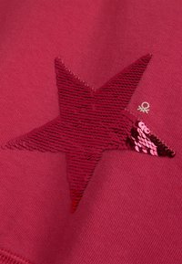 Tessuto rosso con una grande stella realizzata in paillettes reversibili, che passa da un rosso scuro a un rosa lucido all'estremità in basso a destra.