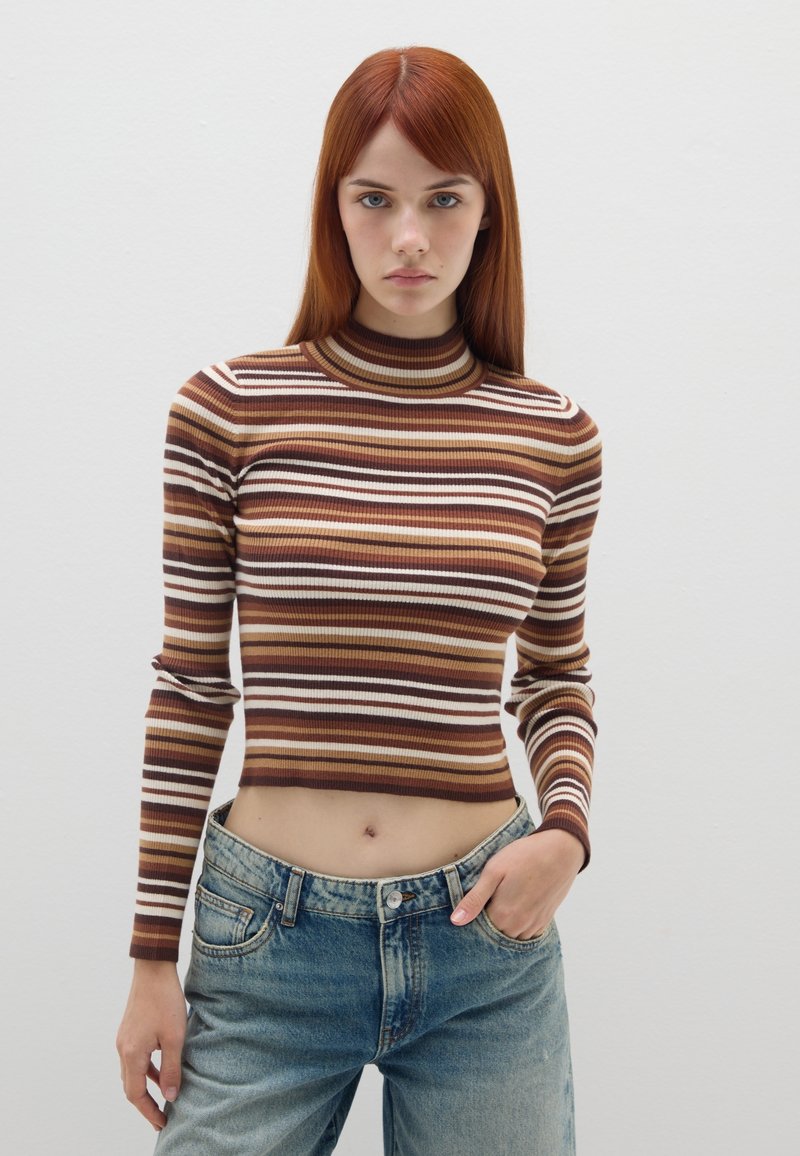 Braun und creme gestreiftes geripptes Rollkragenoberteil, tailliert, kombiniert mit hochgeschnittenen hellblauen Jeans. Minimalistischer Hintergrund.
