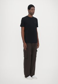 Tricou negru cu mânecă scurtă și guler rotund, asociat cu pantaloni cargo maro, lejerați, care au buzunare laterale și adidași albi.