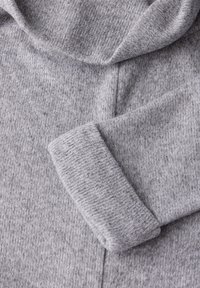 Grauer Hoodie aus weichem, strukturiertem Stoff mit gerippten Bündchen. Das Design umfasst eine große, runde Kapuze und nahtlose Nähte.