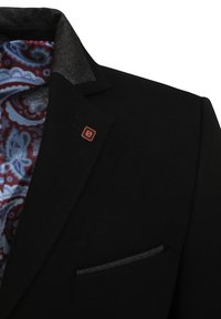 Mustmust ikka tekstureeritud kraega must bleiser, millel on punane logo. Sees on vooder paisleimustriga sinise ja burgundia värviga. Esipooles üks tasku.