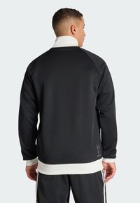 Sudadera deportiva negra con cuello alto, detalle blanco en el dobladillo y textura suave. Presenta mangas raglán y detalle de logo.